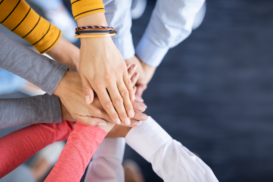 A high-angle, close-up shot of a diverse team stacking their hands together in the centre to show solidarity, unity, and teamwork.